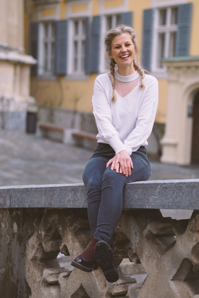 Frau sitzt beim Fotoshooting auf Mauer und lacht frech