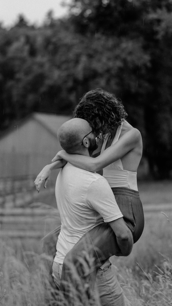 Mann hebt Frau hoch, sie näseln im Regen 