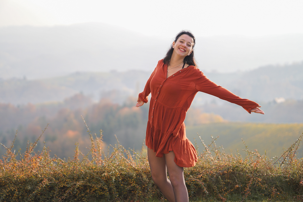 Lachende Frau mit orangem Kleid im Herbst in der Südsteiermark bei Sonnenuntergang mit Weinbergen  